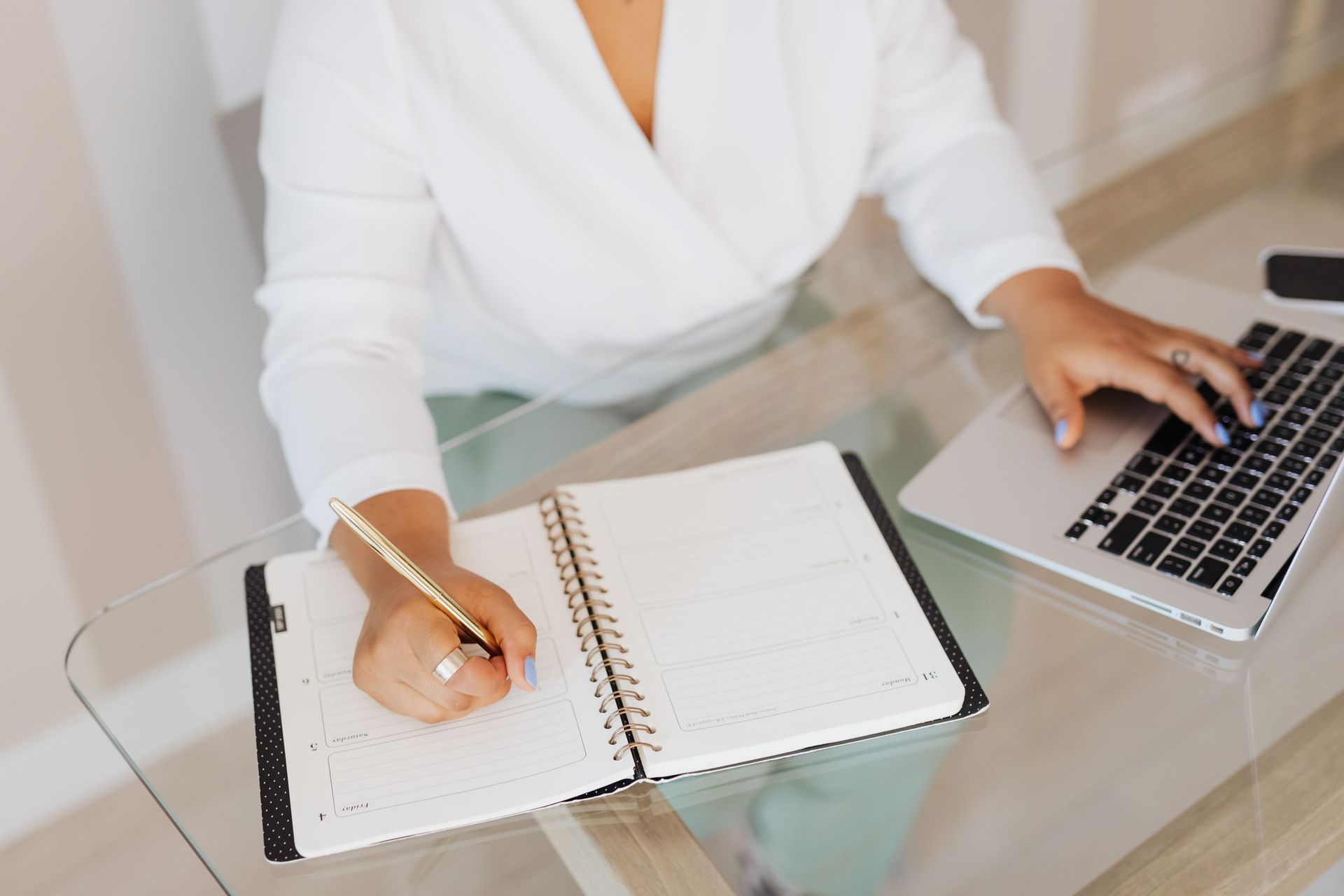 Person writing a monthly budget in a planner next to a laptop